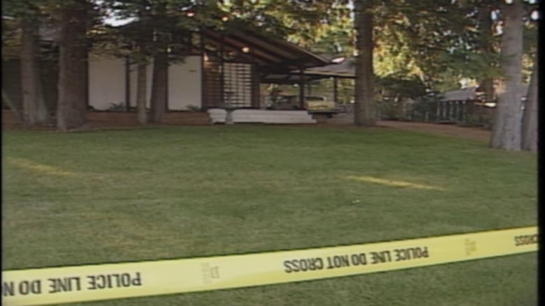 A house is pictured behind yellow police tape. 