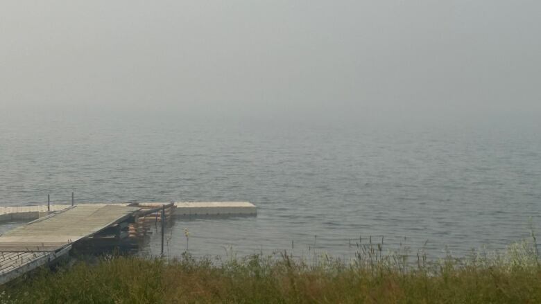 Dock sits on the edge of a lake with the sky covered in wildfire smoke.