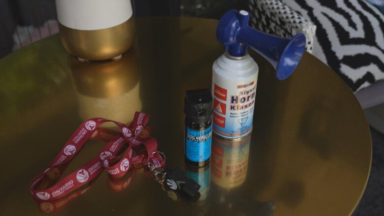 Photograph of an air horn, pepper spray, and whistle on a brown table. 