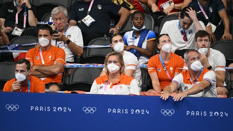 People wearing orange and white uniforms wear respirator face masks while sitting in the stands at the Paris Olympics.