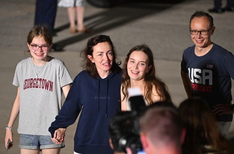 A man and woman walk on a tarmac with two teenage girls, all smiling.