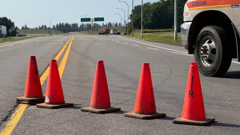 Orange cones show the highway is closed with emergency vehicles in the distance.