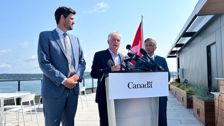 Three men stand around a podium bearing the logo of the Canadian government.