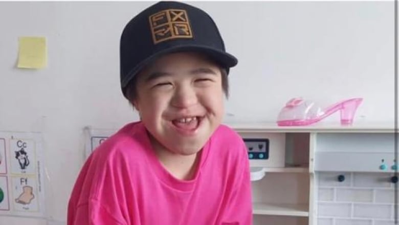 A boy wearing a pink shirt laughs and smiles at the camera. 