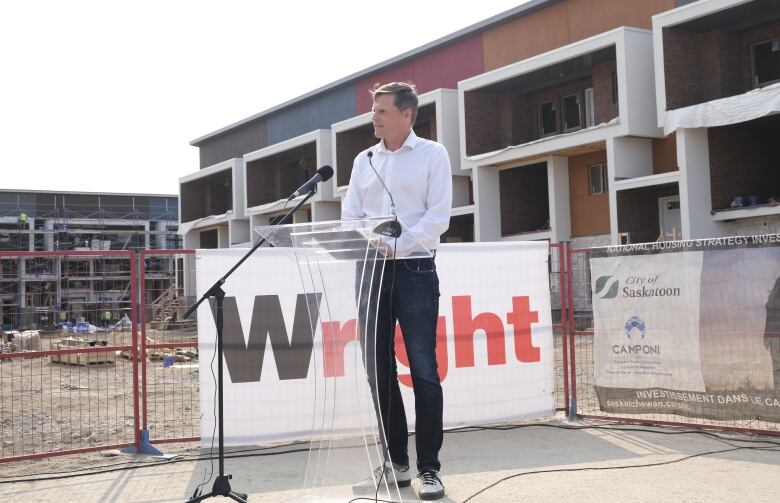 Charlie Clark is speaking at a podium with housing construction in the background