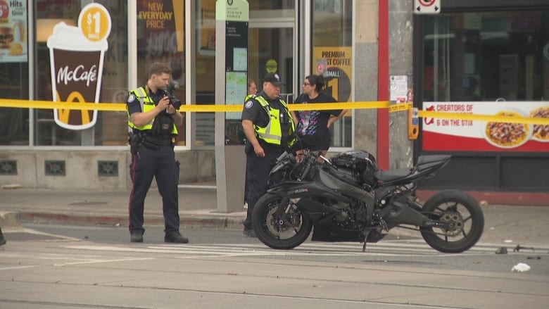 Police in downtown Toronto surrounded by yellow tape taking photographs of a motorbike 