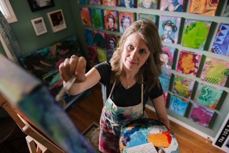 A woman stands painting at an easel.