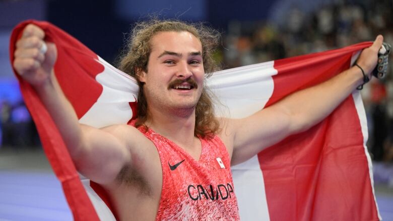 A men's hammer thrower poses with a Canadian flag.