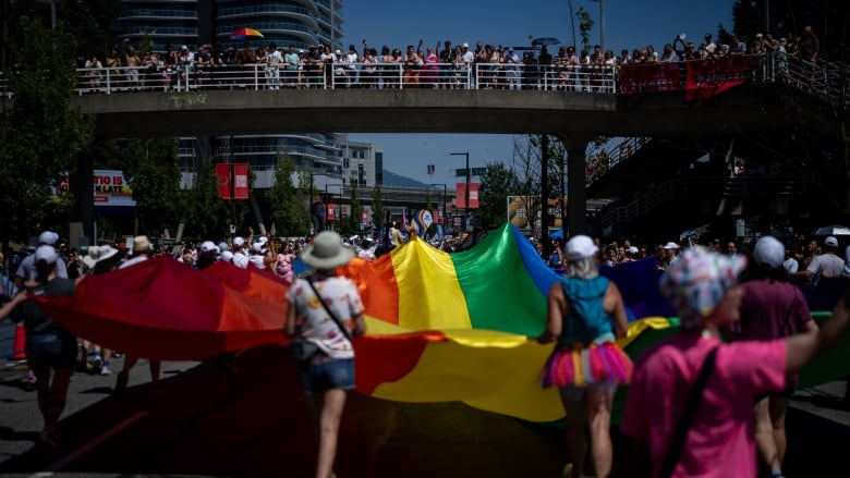 People carry a big rainbow flag while parading across a city road.