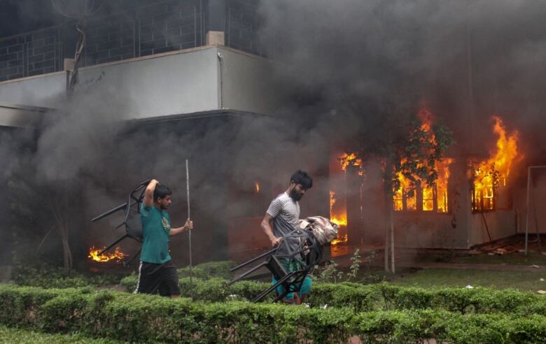 Two men carry looted belongings from a building on fire.