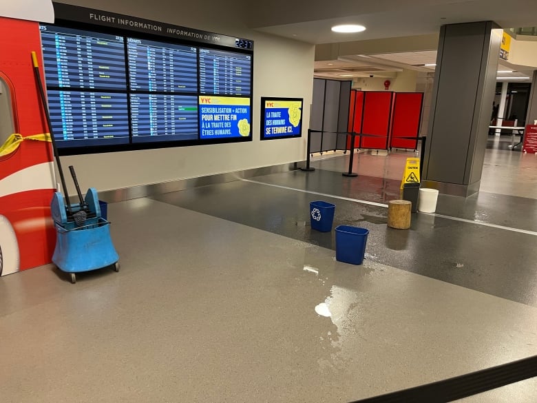 a floor with water on it. buckets and signs are placed around a puddle of water.