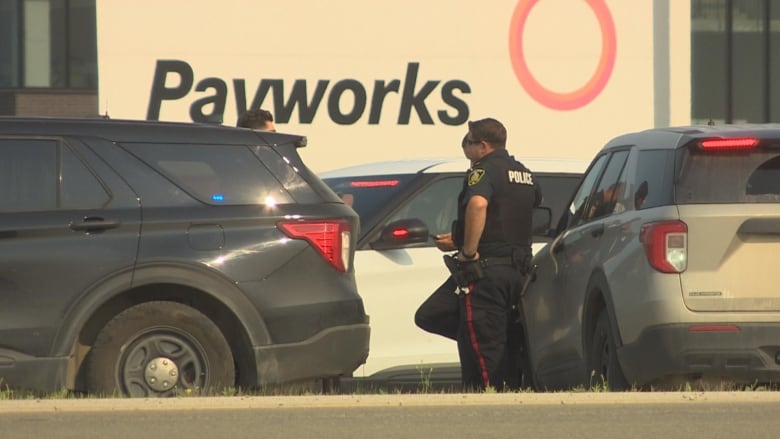 Police officers stand beside a black car