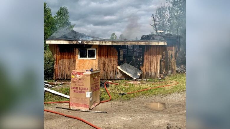 The remains of a burnt log house are seen surrounded by smoke and puddles.