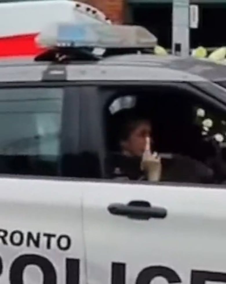 A woman in a police vehicle giving a middle finger out the passenger side window.