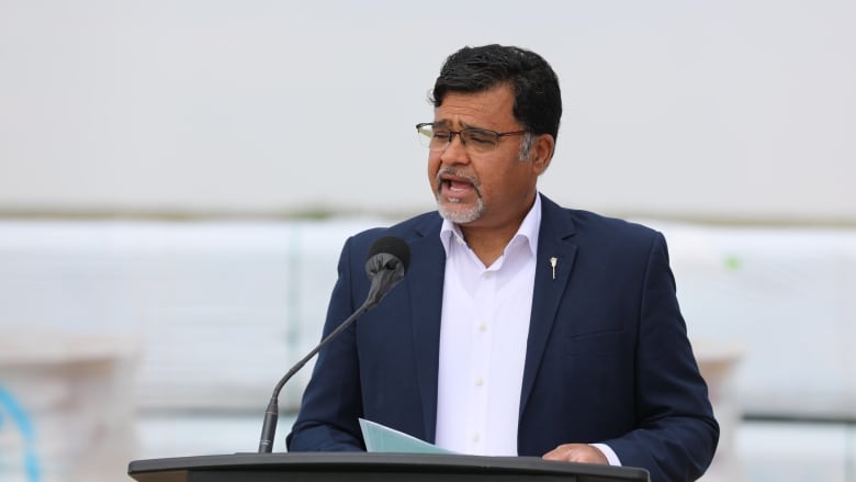 A man in a navy blue suit stands at a podium.