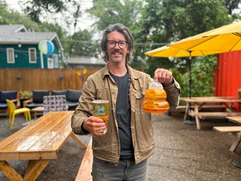 A man holding a cup of beer and a container of beer