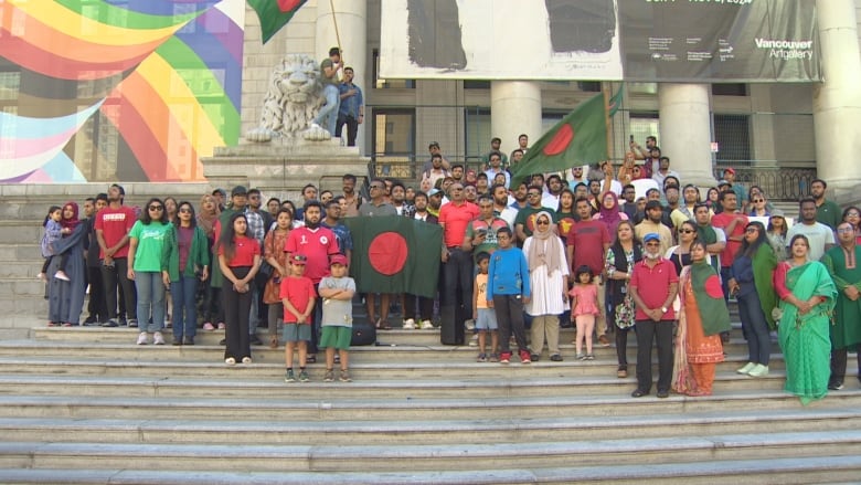 Crowd of people gather at a stair, waving flags outside a building. 