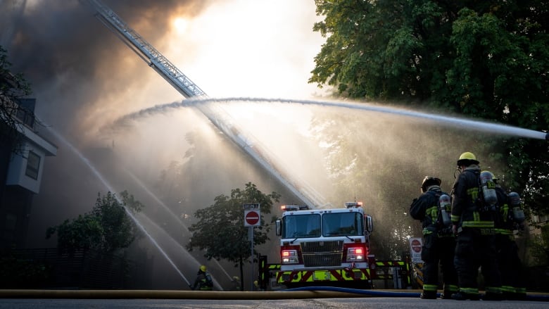 Firefighters and fire trucks are seen spraying water on a building shrouded by smoke.