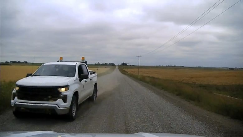 A white car drives on a gravel road. 