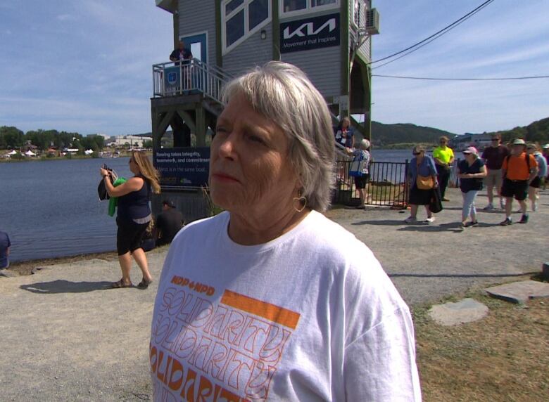 A woman in an NDP t-shirt stands in front of a lake