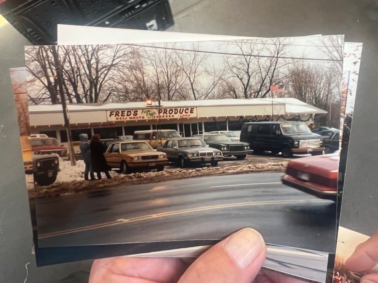 Man shows historical photograph of produce shop with no curbs and a smaller road.