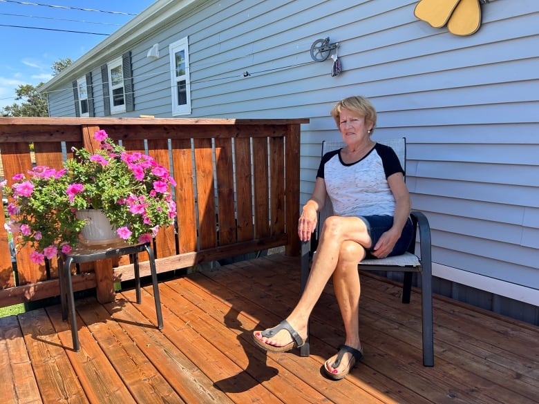 A woman sits on a lawn chair on the shaded deck of a mobile home. 