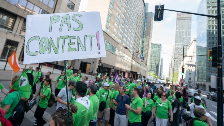 Workers dressed in green striking and carrying a sign reading, 