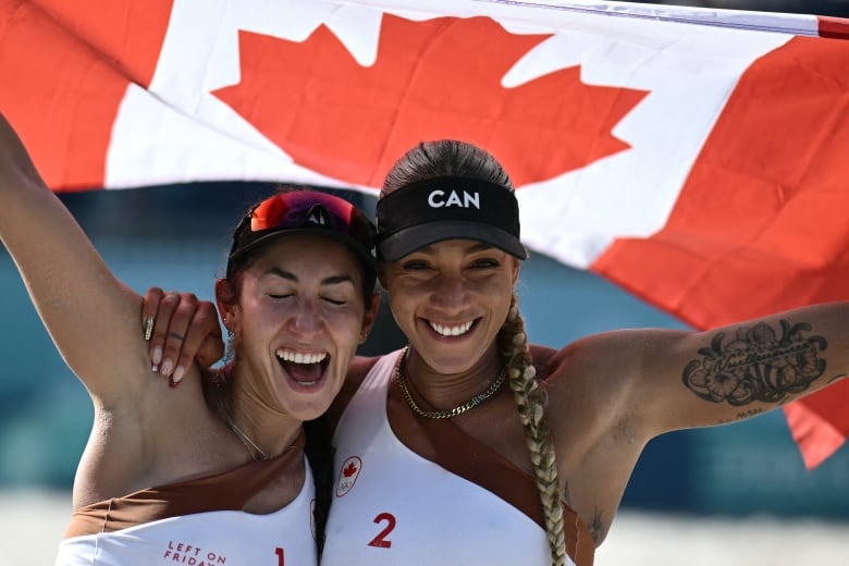 Two female beach volleyball athletes celebrate with the Canadian flag.