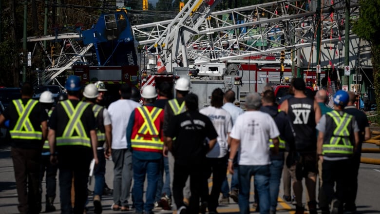 A group of about 20 people approach a crane lying across the road. 