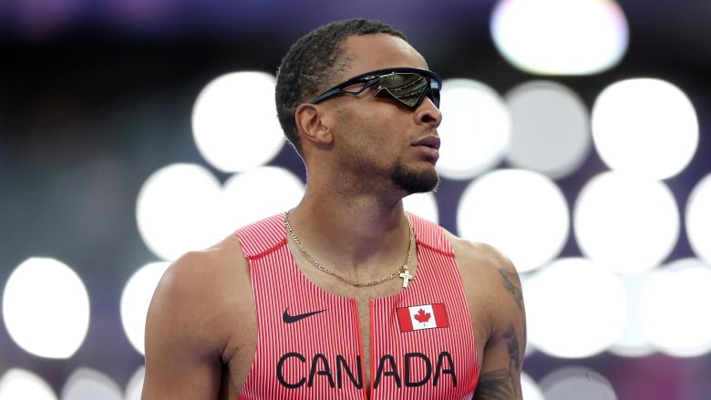 A sprinter looks on as lights flash behind him.