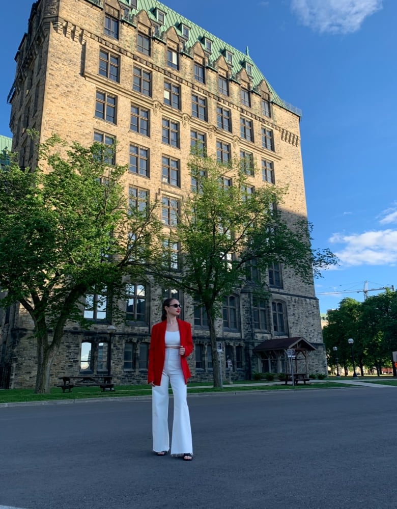 A woman wearing red and white in front of a parliament building.