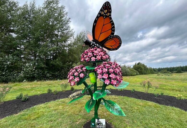 A garden with a monarch butterfly sculpture and milkweed plants.