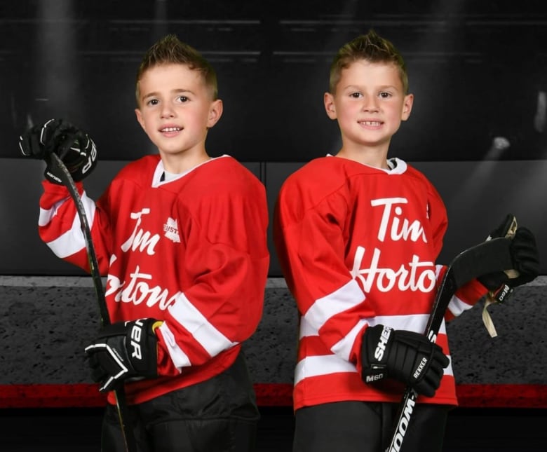 Two identical twins pose for a hockey photo with their sticks and gear.