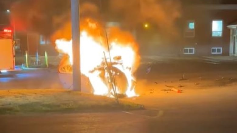 A car engulfed in flames under an electrical pole