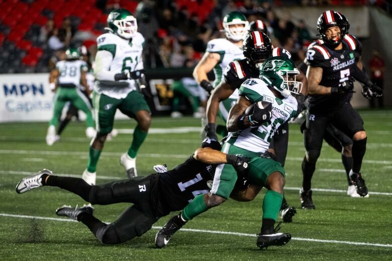 Saskatchewan Roughriders running back Frankie Hickson (20) is tackled by Ottawa Redblacks defensive back Bennett Williams (14) during the second half of CFL action in Ottawa, on Thursday, Aug. 8, 2024. 