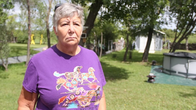 A woman stands facing the camera in what appears to be a backyard.