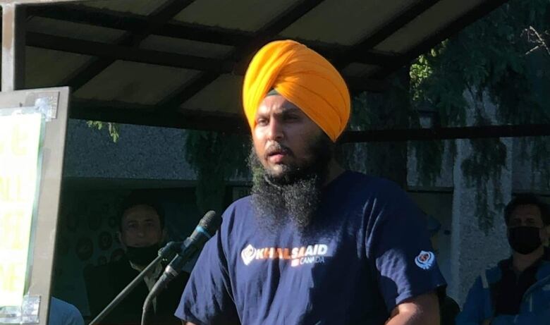 A man in a t-shirt and a turban speaks at a podium.