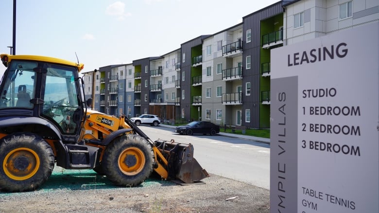 A bulldozer in front of a four-storey apartment building.