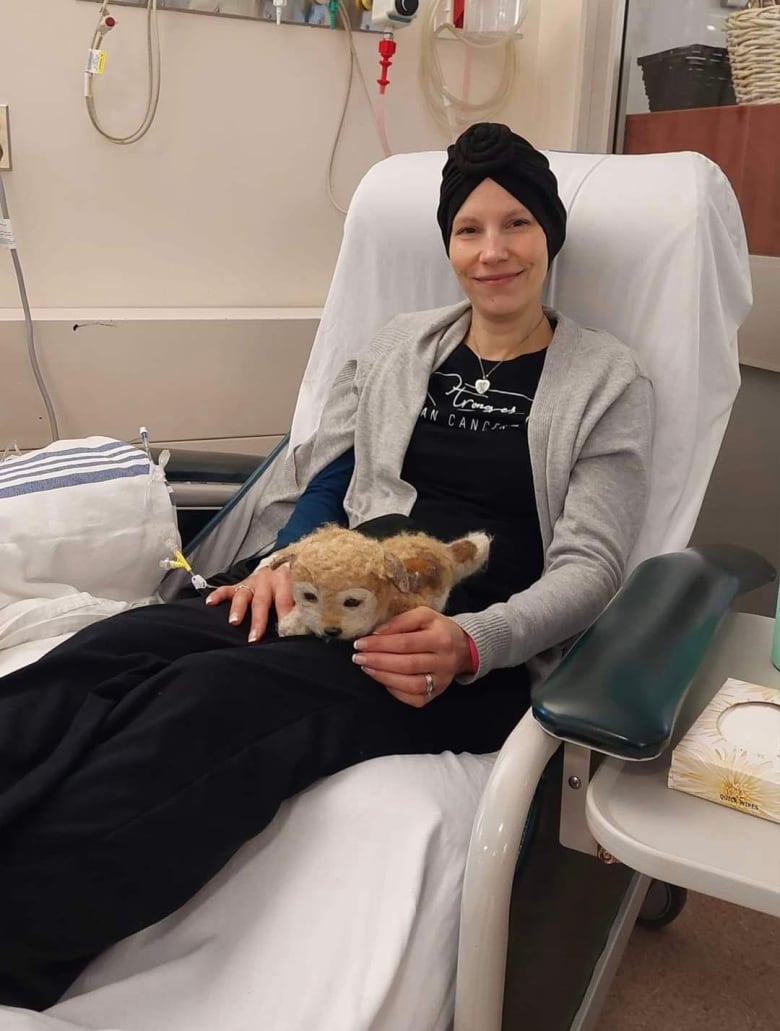 A woman in a turban with a dog in her lap sitting in a long chair inside a hospital.