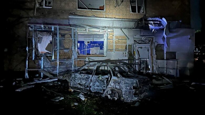 A view shows a destroyed car next to an apartment building that was damaged.