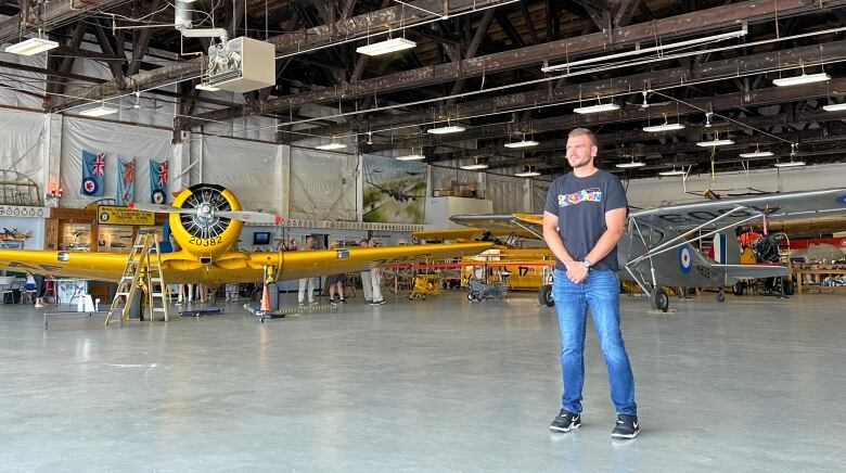 A man stands in an aircraft hangar with historical planes.