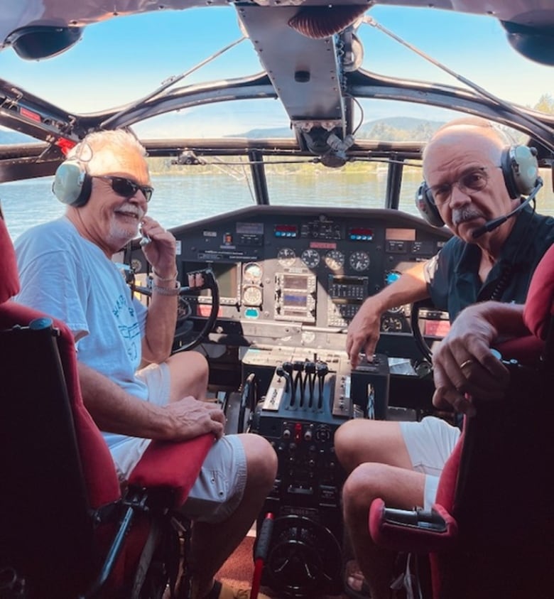 Two elder pilots with headphones inside the cockpit turning back while posing for a photo. 