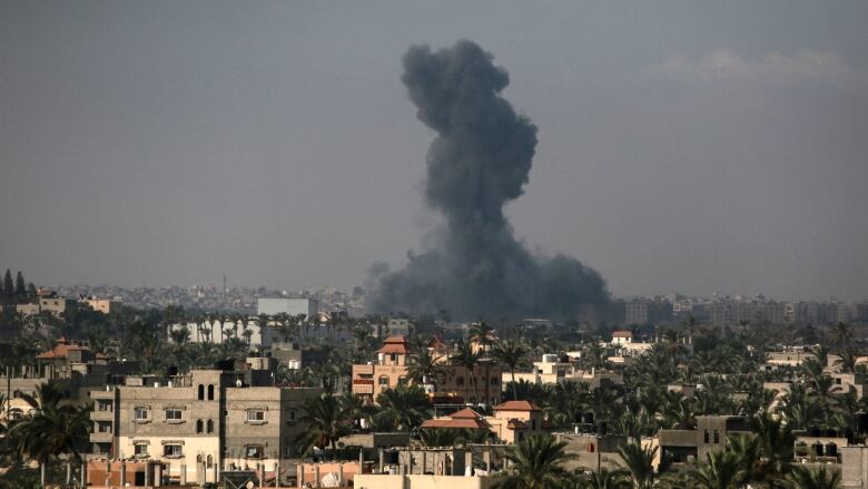 A large black column of smoke rises above a city.