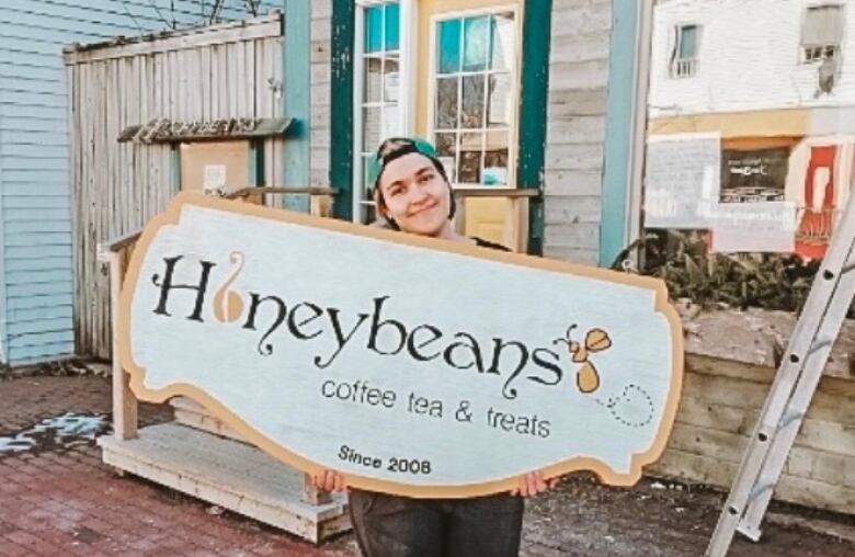 A woman stands in front of a cafe holding a sign.