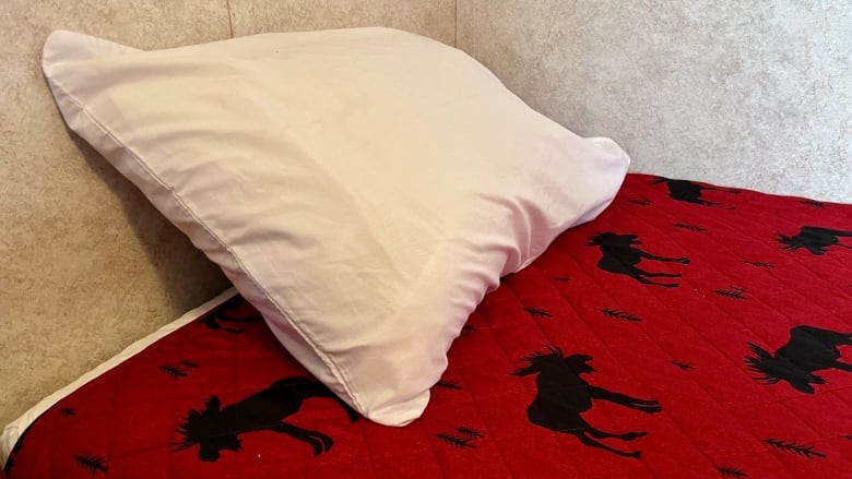 A white pillow sits on a comforter that's red with black silhouettes of moose and pine trees.