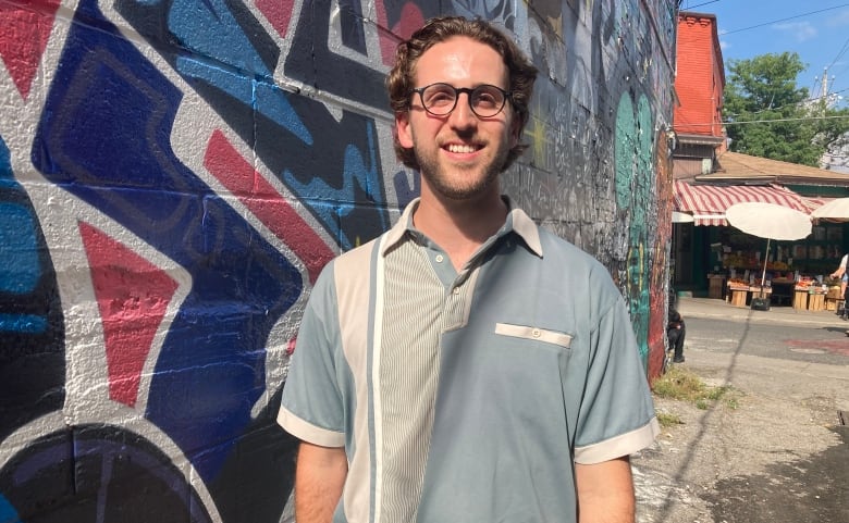 A man wearing glasses and a blue and green polo shirt poses for a photo in Toronto's Kensington Market.