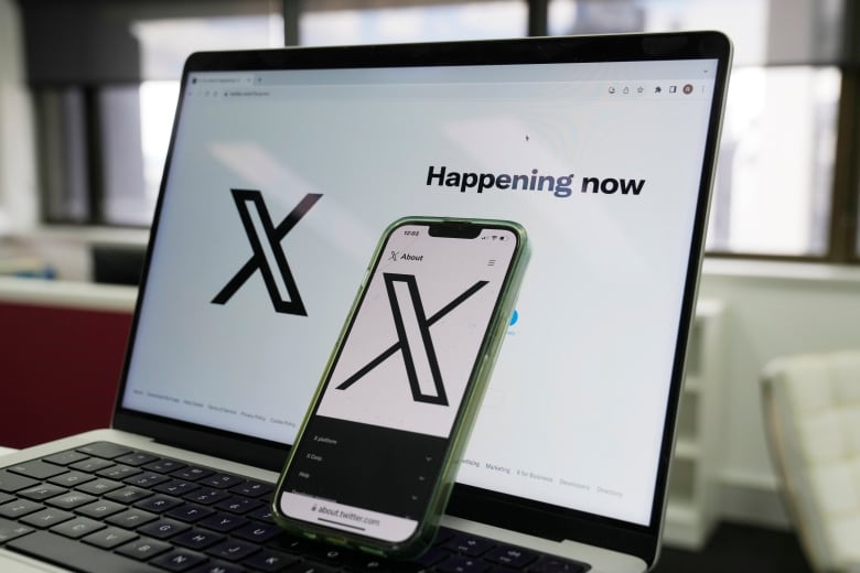 A phone is propped up on a laptop, with the screens of both devices showing an X logo.