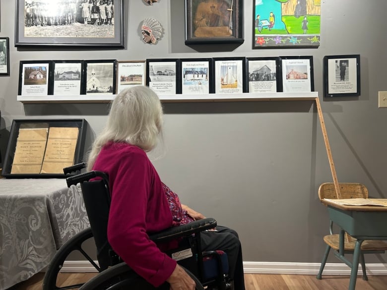 A woman in a wheelchair faces away from camera, toward a wall display of art and information.