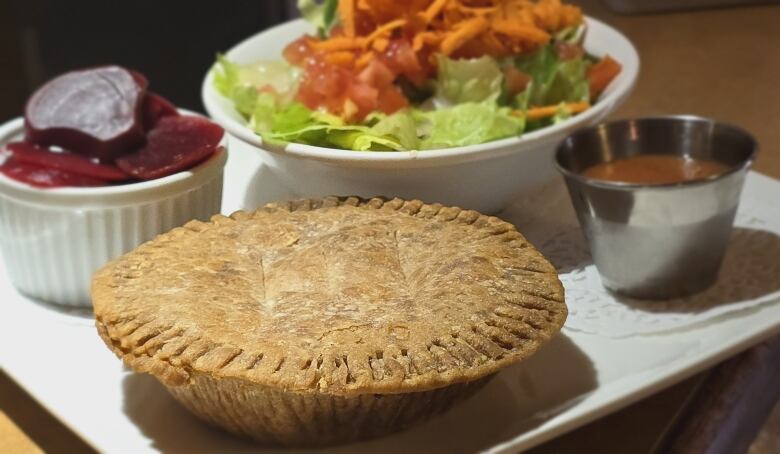 A meat pie on a white plate with side a salad and beets.