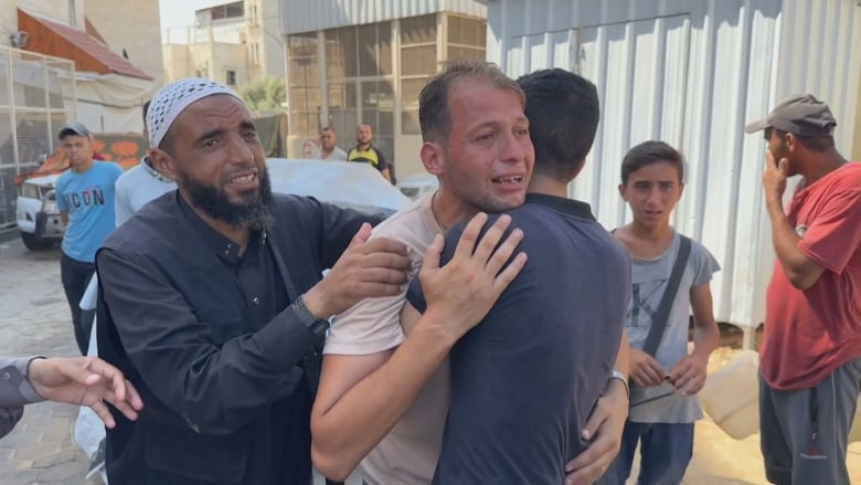 A man wearing a beige shirt is held back by a man in a black shirt